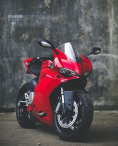 a red motorcycle parked in front of a concrete wall