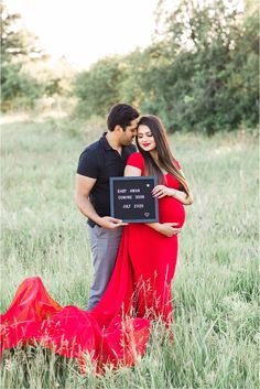 a pregnant couple standing in tall grass holding a sign