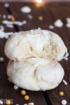 two cookies with white icing and sprinkles on a wooden table next to a lit candle