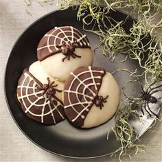 three decorated cookies sitting on top of a black plate next to sprig of grass