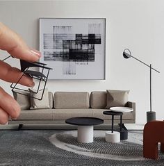 a hand is holding a miniature model of a living room with couches, tables and lamps