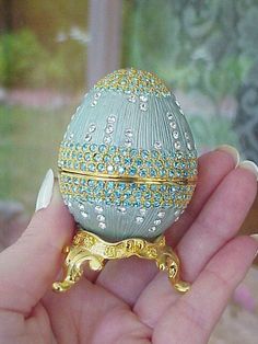 a hand is holding an ornately decorated faber's egg in gold and silver