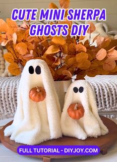 two white ghost towels sitting on top of a wooden plate with fake pumpkins in the background