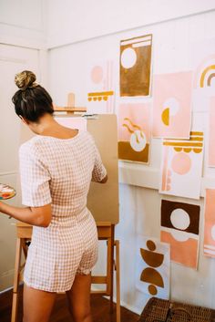 a woman is painting on an easel in front of some art work and holding a plate