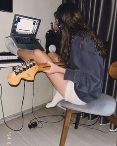 a woman sitting at a desk with a guitar and headphones in front of her