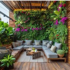 an outdoor living area with lots of plants on the wall and couches in the middle