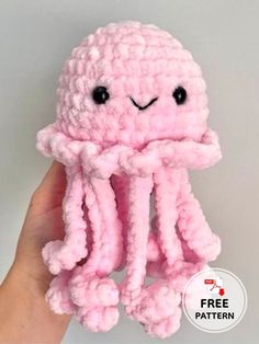 a pink crocheted octopus stuffed animal with black eyes and hands holding it up to the camera