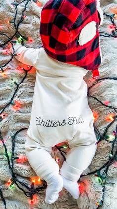 a baby wearing a red and black plaid hat laying on top of a bed covered in christmas lights