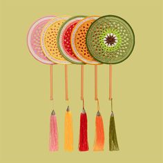 four different colored tassels hanging from hooks on a green background with an orange and yellow circle