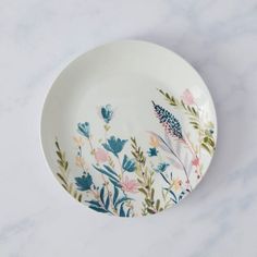 a white plate with colorful flowers painted on the front and sides, sitting on a marble surface