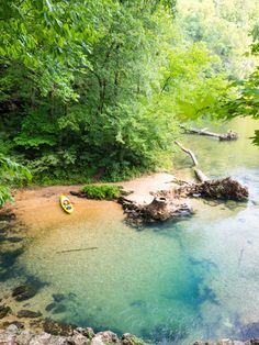 a body of water surrounded by green trees and rocks in the foreground, with two kayaks on it