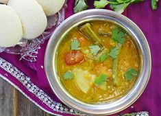 a metal bowl filled with soup next to some cut up vegetables and pita bread