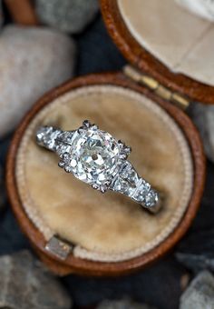 an old diamond ring sits in its box on some rocks and stones, with the rest of it's band visible