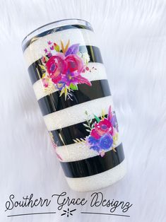 a black and white striped cup with pink flowers painted on it, sitting on a fur background