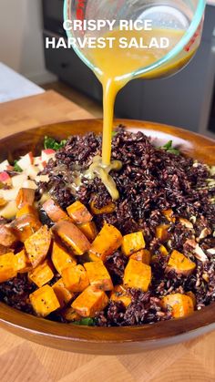 a wooden bowl filled with rice, carrots and other vegetables next to a bottle of orange juice