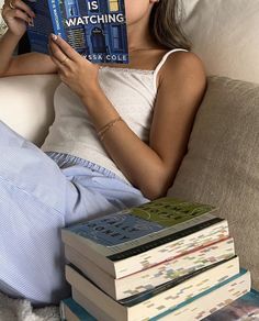 a woman sitting on a couch holding a book in her hand and looking at it