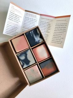 an open box with four different shades of soap in it and a book on the table