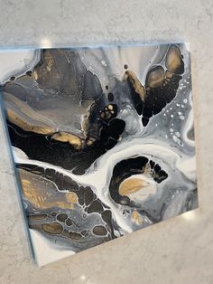 an abstract painting with black and gold accents on a white marble slabd wall in a bathroom