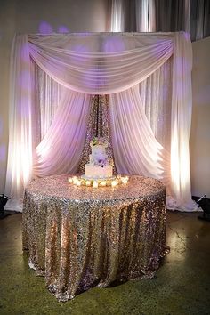 a wedding cake on top of a table under a white drape with candles in front of it