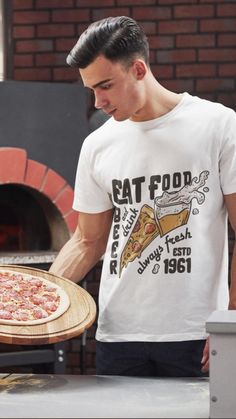 a man holding a pizza in front of an oven