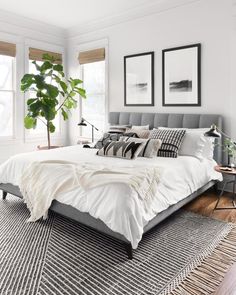 a bed with white sheets and pillows in a bedroom next to two plants on the floor