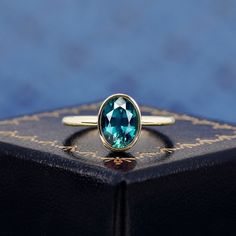 an oval cut blue topaz ring sits on a black box with gold trimming