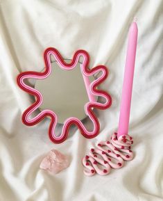 a pink toothbrush holder next to a mirror on a white sheet with some rocks