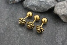 three gold pinecone studs sitting on top of some gray rocks next to each other