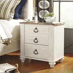 a white nightstand with two drawers on top of it next to a bed in a bedroom