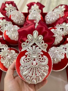 a hand is holding a red ornament with white lace and pearls on it