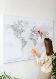 a woman is pointing at a map on the wall with her finger and thumbnails