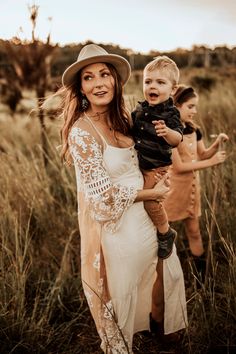 a woman holding a baby in her arms while standing next to two other women wearing dresses and hats