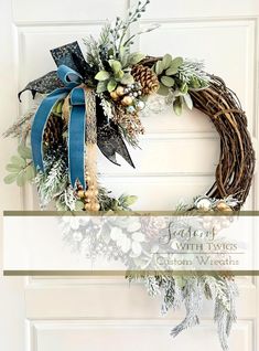 a christmas wreath with evergreen, pine cones and blue ribbon hanging on a white door