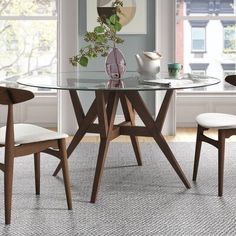 a glass table with chairs around it in front of a window and potted plant