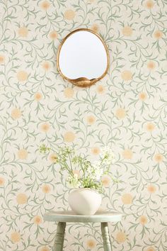 a white vase with flowers sitting on top of a table next to a wall paper