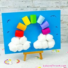 a rainbow made out of cotton balls sitting on top of a easel with a blue background