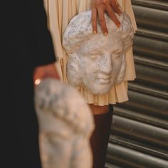 a close up of a person's hand on a statue holding a stone head