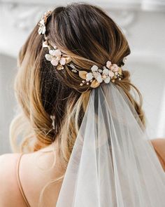 a bride wearing a veil with flowers on it's head and hair comb in her hair