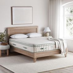 a bed with a wooden headboard and mattress in a room next to a window