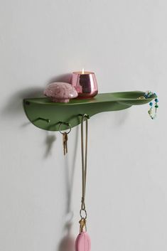 a green shelf with some pink items hanging from it's sides and a candle on top