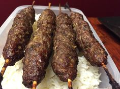 several skewers of meat on top of rice in a plastic container with tongs