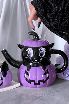 a purple pumpkin shaped teapot with a black cat on it