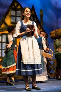 a woman standing on top of a stage holding a book in front of other people