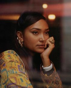 a woman sitting in front of a window with her hand on her chin