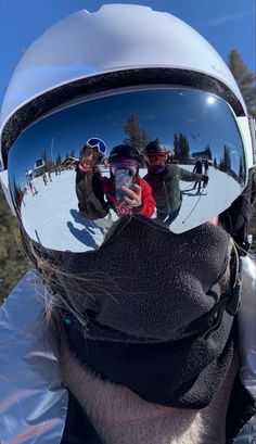 the reflection of three people in their ski goggles is seen through the lens of another person's helmet