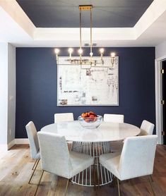 a dining room table with white chairs and a painting on the wall in the background