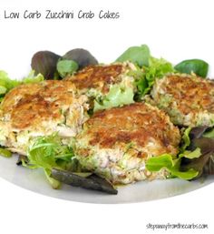 two crab cakes on a plate with lettuce and olives next to it