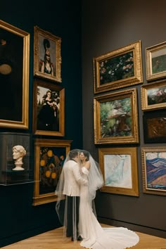 a bride and groom are kissing in front of paintings on display at the art museum