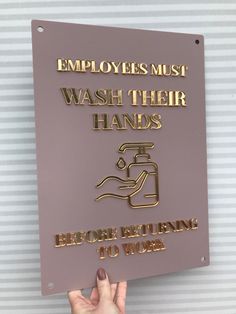 a hand holding up a sign that says employees must wash their hands before entering to work