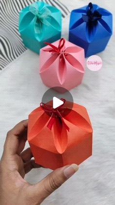 someone is holding three different colored boxes with bows on them, and the video below shows how to fold an origami box